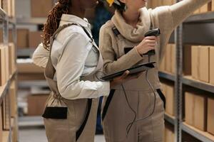 Storehouse colleagues reaching for cardboard box on shelf to scan barcode. Warehouse operators managing received parcels registration with bar code scanner and digital tablet software photo