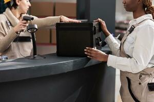 Warehouse reception worker scanning product and checking price for inventory. Two diverse women storehouse colleagues doing black box goods stock management at counter desk photo