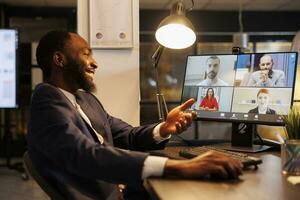 Smiling executive manager having remote conversation with team discussing marketing strategy during online videocall meeting. Diverse coworkers working at company growth report in office photo