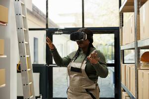 Storage room employee wearing virtual reality headset, enjoying warehouse simulation, preparing customers orders in storehouse. African american supervisor working at merchandise inventory photo