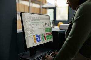 African american worker analyzing goods logistics on computer, working at merchandise inventory in warehouse. Storage room supervisor checking customers orders during products quality control photo