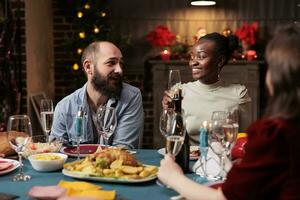 Young person raising glass for speech during christmas eve holiday at home, gathering with friends and family to eat traditional homemade food and give toast at table. Festive people. photo