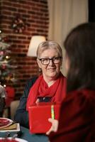 Woman giving present to her mother at christmas dinner celebration, feeling cheerful during december celebration. Family exchanging gifts and enjoying good time at home with people. photo