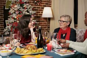 alegre grupo de personas disfrutando Navidad víspera fiesta a hogar, joven y antiguo familia miembros teniendo divertido comiendo hecho en casa comida y Bebiendo alcohol. amigos reunión alrededor festivo cena mesa. foto