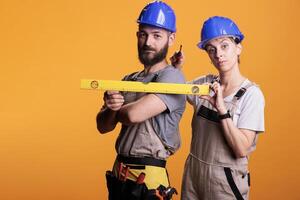 Construction workers holding screwdriver and water level in studio shot, using ruler or leveler to work on renovation. Team of building experts being confident with renovating tools. photo