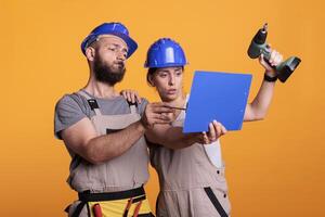 Team of construction workers analyzing papers on clipboard, taking notes of measurements. Builders looking at files with building or renovating information, engineering skills with power drill. photo