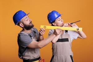 Contractors holding screwdriver and water level tool in studio shot, using ruler or leveler to work on renovation. Team of building experts being confident with renovating tools. photo