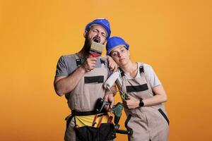 Team of tired renovators working with construction tools, falling asleep after renovating project. Man and woman builders holding power drill, painting brush or roller and pair of pliers. photo