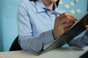 Female entrepreneur concentrating on writing in files and signing documents and papers about project on a clipboard. Woman sitting at office desk looking at statistics and finishing paperwork. photo