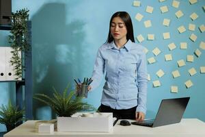 Employee collecting things from the office after resigning from her job due to disagreement with employment conditions. Woman with cardboard box on table keeping personal belongings. photo