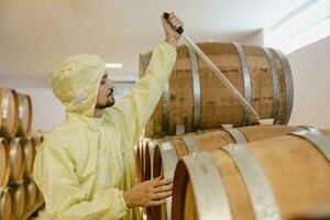 wine maker specialist worker work in win factory test wine taste aroma fermentation in oakwood barrel tank. photo