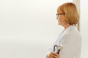 doctor stress. senior medical staff female with stethoscope looking out serious worry thinking. photo