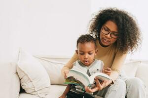 educación madre dando aprendizaje a pequeño chico niño interesante a leer el libro para inteligente niño, africano negro personas familia foto