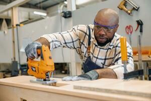 black african male carpenter joiner using Jig Saw wood panel cutter to cut making furniture panel in workshop photo