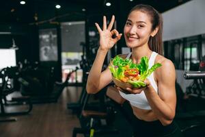 sport healthy beautiful asian woman showing vegetables mix salad for diet food low calories in fitness sport club photo