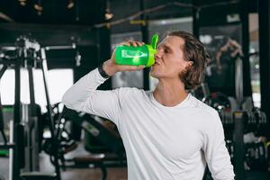 sano deporte hombre con suero criba vibradora botella. contento Bebiendo suero proteína para músculo fuerza masa ganancia y bajo grasa bebida comida en gimnasio aptitud foto