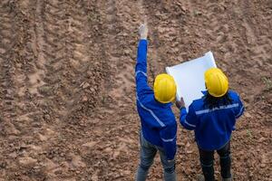 Land surveyor team standing working together at construction field consult study looking building location with floor plan photo