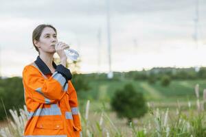 Engineer woman technician standing relax rest drinking clean water after finish service maintenance wind turbine power generator photo