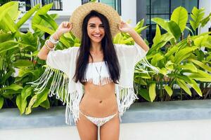 Close up positive portrait of cheerful woman in straw hat and white boho fringed beach cover up.  Holidays and tropical vacation concept. photo