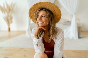 Close up portrait of Pretty blond woman in straw hat   chilling at home. Stylish modern bedroom in boho style. photo