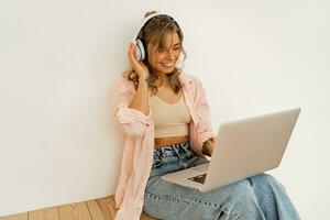 Pretty blond female  student  using lap top , listening online course by lap top and sitting on the floor in living room photo