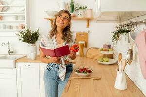 Pretty girl  looking at recipe in cookery book preparing vegetable salad cooking food in light kitchen at home. Dieting healthy lifestyle concept. photo