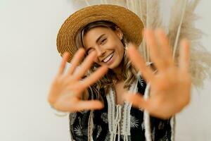 Playful cheerful woman in straw hat pull hands to the camera.  White background.  Boho outfit. Stylish summer accsesorises. photo