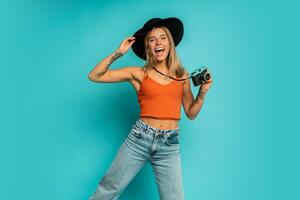 Young pretty  traveling girl with blonde hair  jumping  over   turquoise  wall. Wearing  color  summer  clothes . Holding vintage camera.  Vacation mood. photo