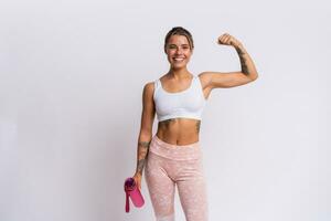 Fit blond woman with perfect smile in stylish sportswear looking at camera and holding bottle of water over white background. Demonstrate muscles. photo