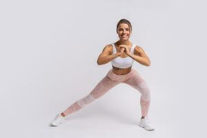 Athletic   blond woman with perfect smile training muscles of hands and legs. Photo of woman in stylish sportswear isolated on white background.