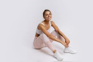 Fitness and lealthy lifestyle concept. Happy sporty young woman sitting on the floor at studio after exercising, resting and looking at camera. White background. photo