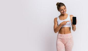 Training app. Fit pretty woman showing smartphone with modern fitness application for tracking sports  activity. Posing over yellow studio background. photo