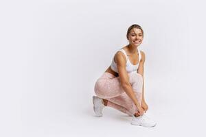 Fitness and lealthy lifestyle concept. Happy sporty young woman sitting on the floor at studio after exercising, resting and looking at camera. White background. photo