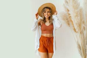Boho mood. Stylish woman in summer outfit with straw hat posing over white background in studio with pampas grass decor. photo