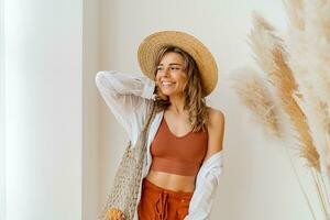 Studio portrait of beautiful blond woman with perfect smile holding eco friendly mesh shopper with fresh  vegetables. photo