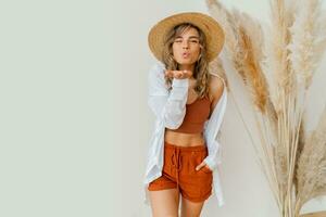 Boho mood. Stylish woman in summer outfit with straw hat posing over white background in studio with pampas grass decor. photo