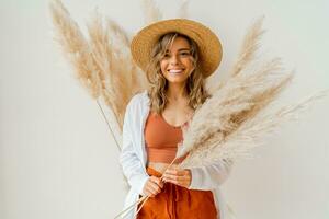 Close up portrait of smiling  blond woman with perfect smile in stylish boho autfit. Posing in inerior studio over white background. photo