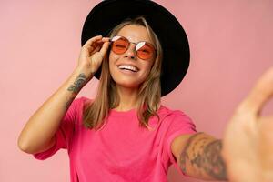 cerca arriba estudio foto de sonriente joven mujer con tatuaje en manos posando terminado rosado antecedentes.