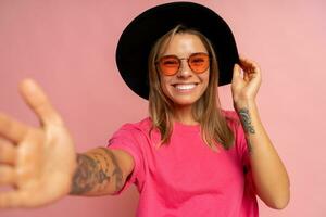 cerca arriba estudio foto de sonriente joven mujer con tatuaje en manos posando terminado rosado antecedentes.