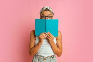 Studio photo of pretty blond  student woman with suprice face posing with note book on pink background.