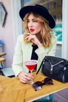 elegante mujer en casual verano atuendo en negro sombrero sentado en moderno café y Bebiendo cóctel. foto