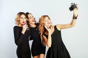 Group of best friends, three elegant  girls in black luxury dress making self portrait , drinking red wine , posing on white background. photo