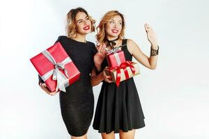 Two cute celebrating woman holding big new year gift boxes. Surprise faces. Wearing elegant black dress. photo