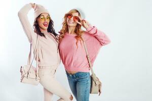 Two blissful girls in pink trendy  outfit   posing in studio on white background. Cute friends having fun , walking, jumping, photo