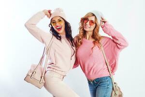 image of two girls, happy friends in stylish pink clothes and hat spelling funny  the together. White background. Trendy hat and glasses.Showing peace. photo