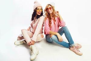 Two  laughing girls, best friends posing in studio on white background. Trendy pink winter outfit. photo