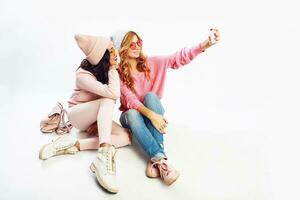 Two fashionable miling girls making self portrait. White background. Pink  clothes. photo