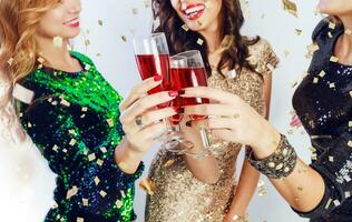 Party and holidays concept. Three glamour women in luxury glitter sequins dress drinking cocktails  and having fun. Hollywood make up, wavy hairstyle. White background. photo