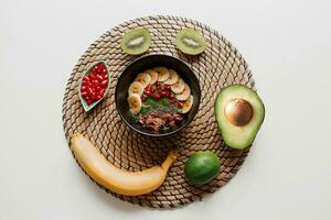 Overhead view on plate of green smoothie bowl topped with avocado and spinach , pomegranate seeds and granola. White background. photo