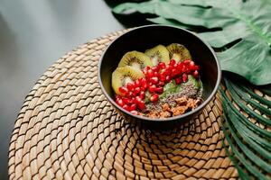 Healthy food concept. Top view on table with smoothie bowls.  Plate topped with kiwi, granola, garnet, chia, avocado. Tropical leaves on background. Copy space. photo